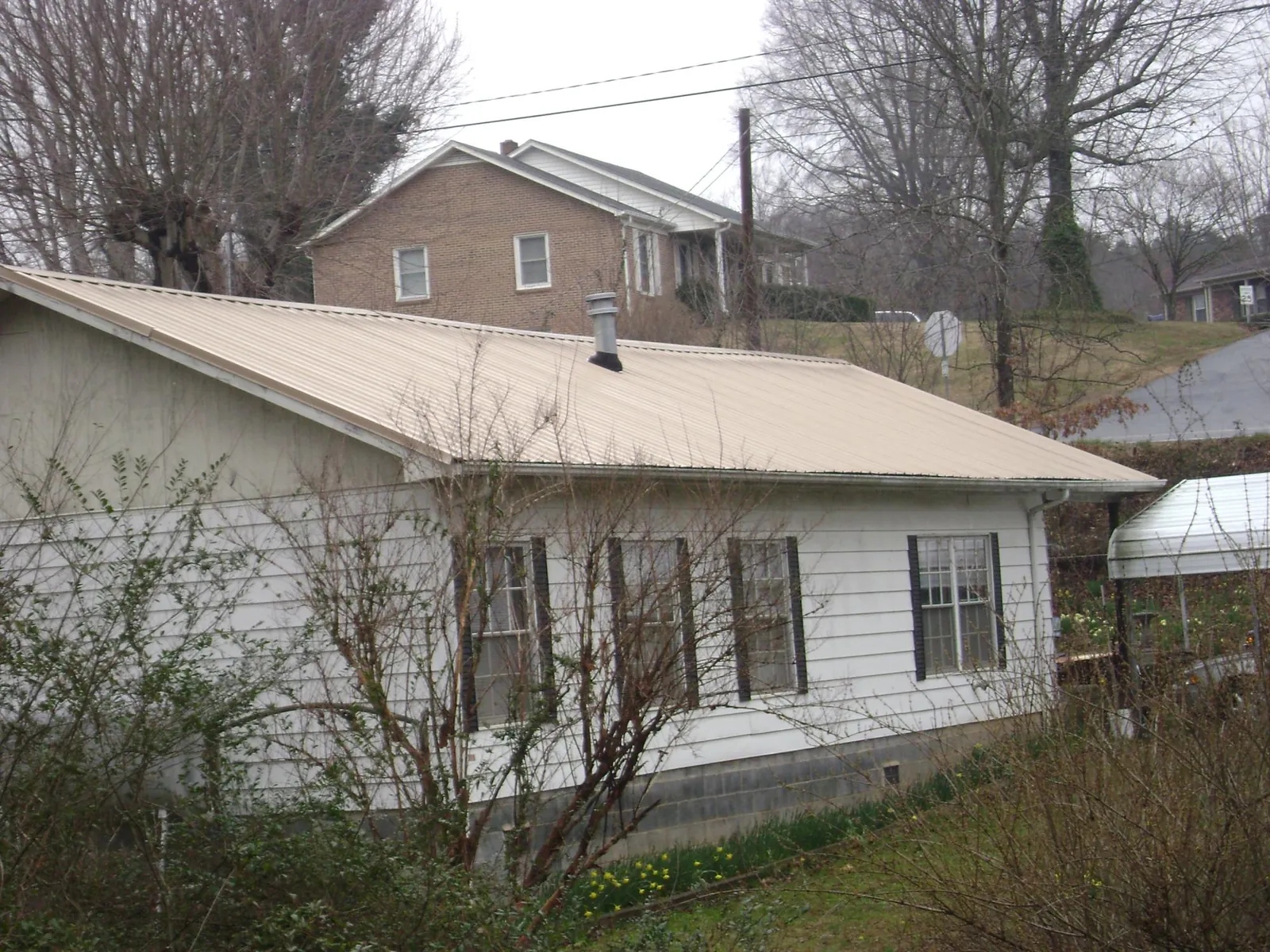 Tan metal roof on a white sided house set into a hillside — Commercial Roofing by Roofing Brothers in Preston